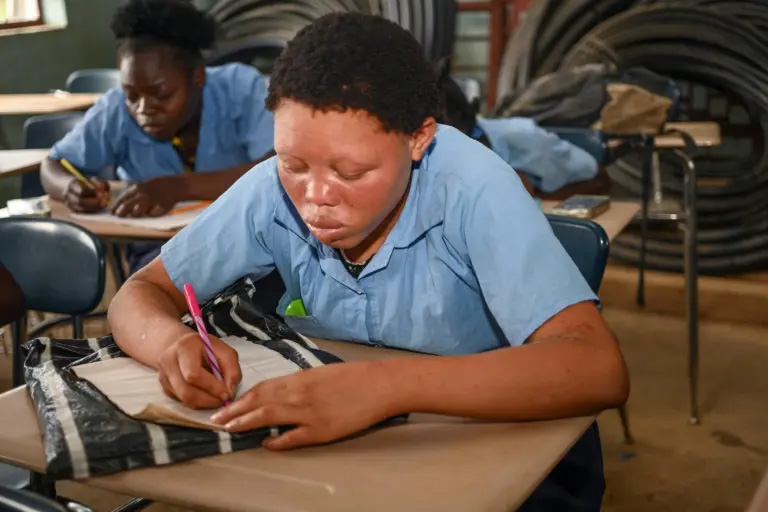 A male student in a classroom, working on his notebook. Photo provided by World Vision.
